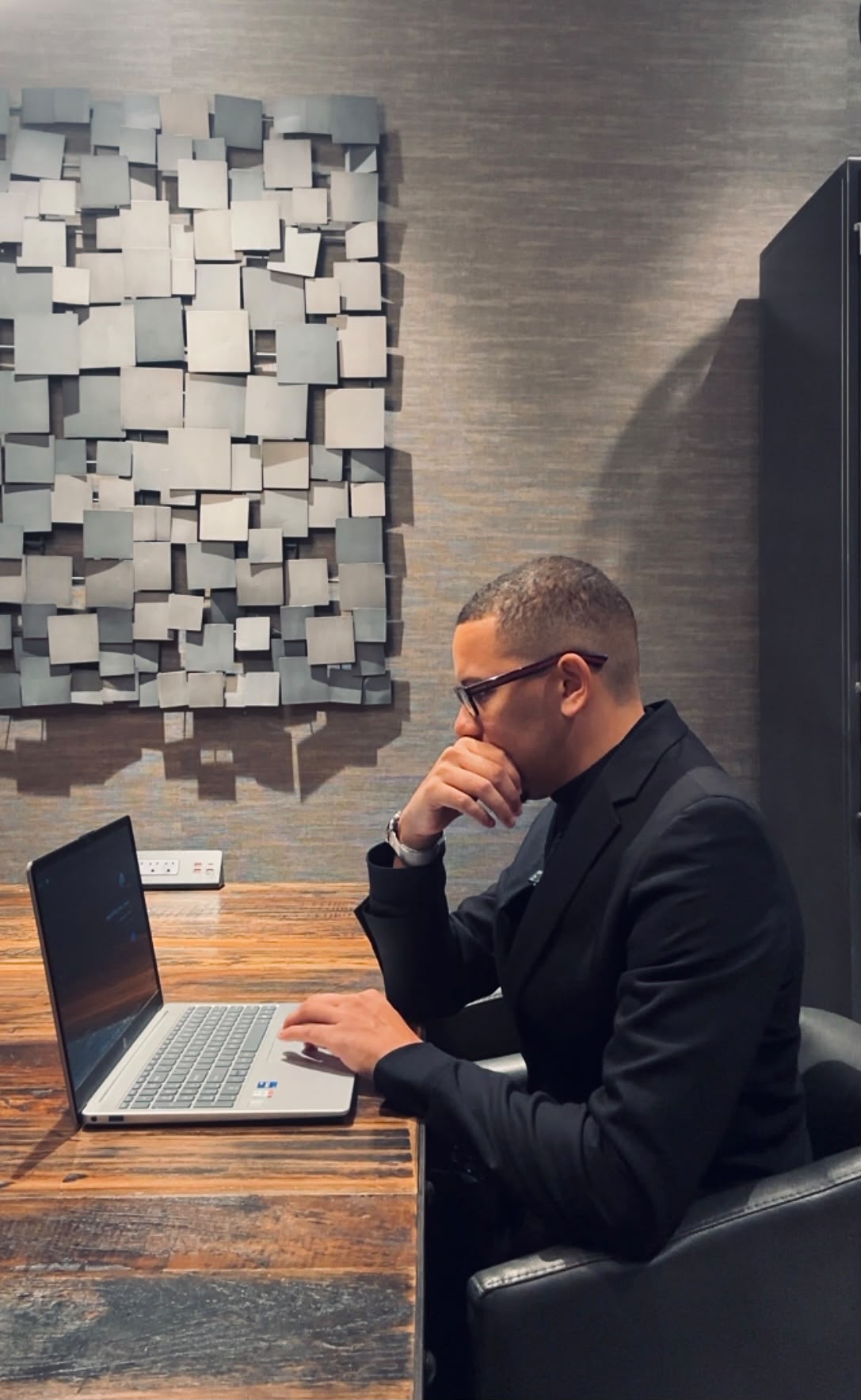 A mentor seated at a desk in profile, focused on his laptop in a modern office